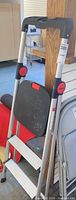 Full view of Benchmark aluminum step ladder folded against post