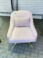 Front view of blush pink velvet swivel armchair with pillow and brass base