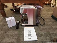 Espresso machine with portafilter, boxed milk jug, manual on carpet
