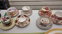 Seven assorted floral bone china teacup and saucer sets displayed