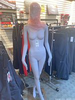 Front view of full-body mannequin with bubble-wrapped head and clothing racks in background