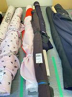 Five rolled fabric bolts in assorted colours and prints on table