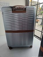 Front view of silver MAT suitcase showing textured shell and brown accent