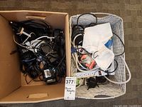 Cardboard box and wicker basket containing tangled power adapters, loose cables, power strips