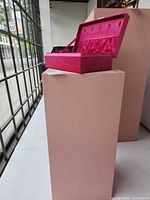 Overall view of pink pedestal stand with box on top