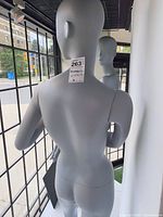 Rear view of one gray mannequin showing matte finish, tag, base attachment point
