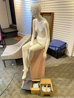 Mannequin seated on pink pedestal with extra heads in boxes visible