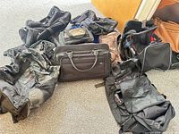 Group view of eight assorted duffel bags and laptop briefcases laid on floor