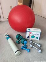 Group shot showing red exercise ball, boxed kit, yoga mat, three pairs dumbbells