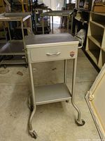 Full view of GOMCO metal medical cart with drawer, shelf and casters