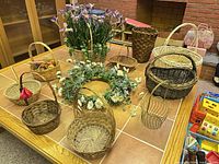 Overview of assorted wicker baskets, faux iris planter, tall basket and wreath on table