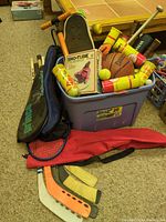 Overall view of tote with basketball, skateboard, sled box, tennis ball cans, racket, hockey blades