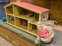 Overall view of wooden dollhouse exterior and bag of doll clothing