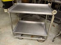 Full view of stainless steel two-tier cart showing shelves, frame, wheels