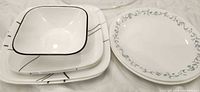 Stack of Corelle square plates, square bowl, and Corelle round plates showing both patterns