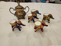 Group shot showing six elephant tealight holders with candles and metal lidded pot