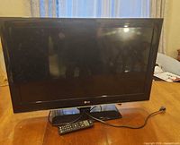 Front view of LG TV on stand with remote and power cord visible