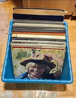 Bin containing stack of LPs, front album John Denver’s Greatest Hits visible