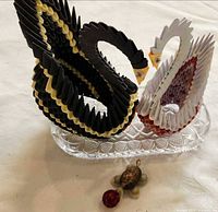 Pair of origami swans on glass dish with shell turtle ornament in foreground