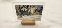 Front view of signed winter cabin watercolor in acrylic frame on wooden stand