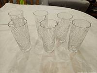 Six clear cut crystal highball glasses grouped on cloth surface.