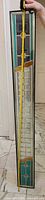 Full view of narrow stained glass panel standing upright with tape measure showing height