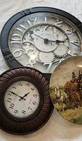 Three clocks laid out: black gear clock, brown ridged clock, ceramic plate clock