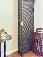 Folded four-panel dark brown woven synthetic wicker room divider leaning against wall