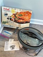 Hamilton Beach slow cooker with glass lid, paperwork, kitchen twine and boxed T-fal roaster shown together