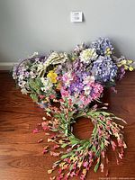 Group of silk flower arrangements, baskets and wreath against wall