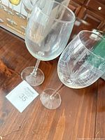 Two wine glasses shown: one plain clear, one etched pattern, demonstrating styles