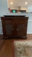 Front view of dark brown solid wood cabinet with two louvered doors and open lift-top section
