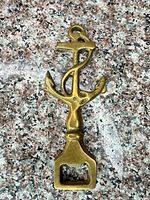 Front view of brass anchor bottle opener showing opener end, anchor shape, patina