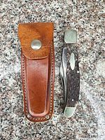 Closed knife beside leather sheath on granite surface