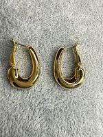 Pair of gold tone oval hoop earrings on grey background