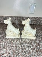 Two off-white SyrocoWood Scottish Terrier dog bookends on countertop
