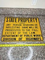 Full view of yellow cast metal State Property sign on countertop with measuring tape showing dimensions