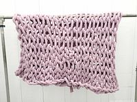Full view of mauve pink chunky knitted blanket hanging, showing overall size and color