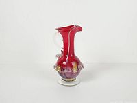 Full view of cranberry glass pitcher showing shape, handle, ruffled band and foot