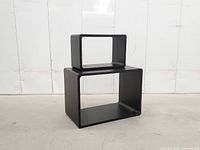 Both black hollow cube side tables, large on floor, small on top