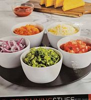Box showing five white bowls with condiments on round tray
