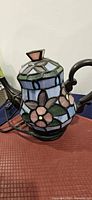 Side view of stained glass teapot lamp showing floral panels and cord