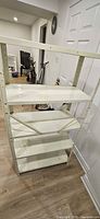 Full view of white metal shelving unit showing four shelves, uprights and cross-brace