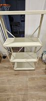 Full view of off-white metal shelving unit showing three shelves and frame