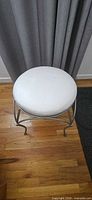 Full view of metal stool showing white round cushioned seat and curved metal legs