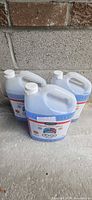 Three sealed jugs of blue winter windshield washer fluid standing on concrete