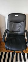 Front view of black faux-leather rolling office chair showing seat, back, armrests and base