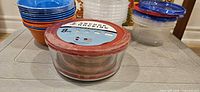 Front view showing Anchor Hocking set, stack of orange/blue bowls, clear bowls with lids, clear container with blue lid