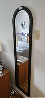 Front view of tall arched black-framed mirror reflecting bedroom interior