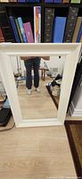 Front view of rectangular mirror with white wooden frame leaning against wall